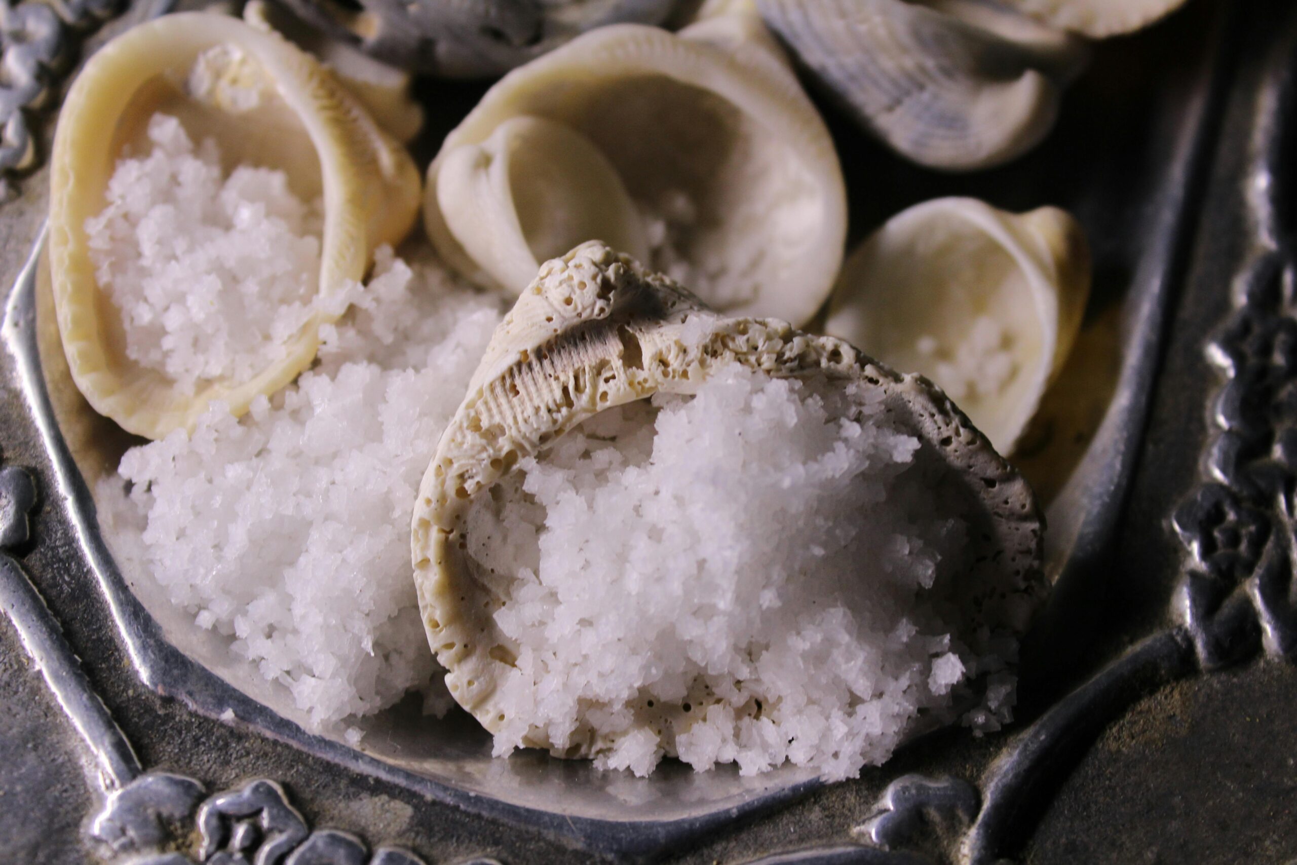 Coarse sea salt fills delicate seashells placed on an ornate silver tray, creating a coastal and artisanal aesthetic