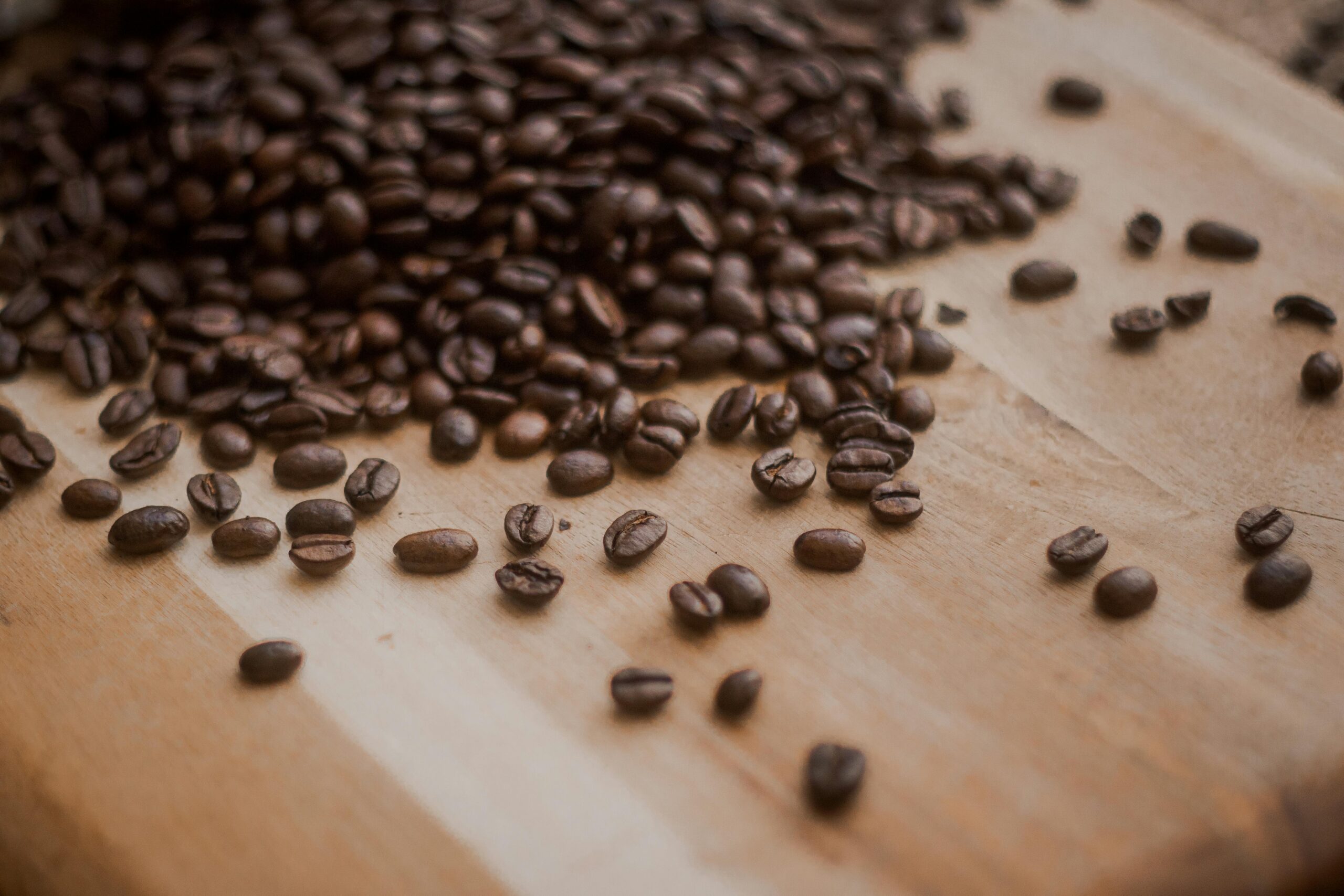 Roasted coffee beans scattered across a wooden table, highlighting the different shapes and shades of brown in the beans