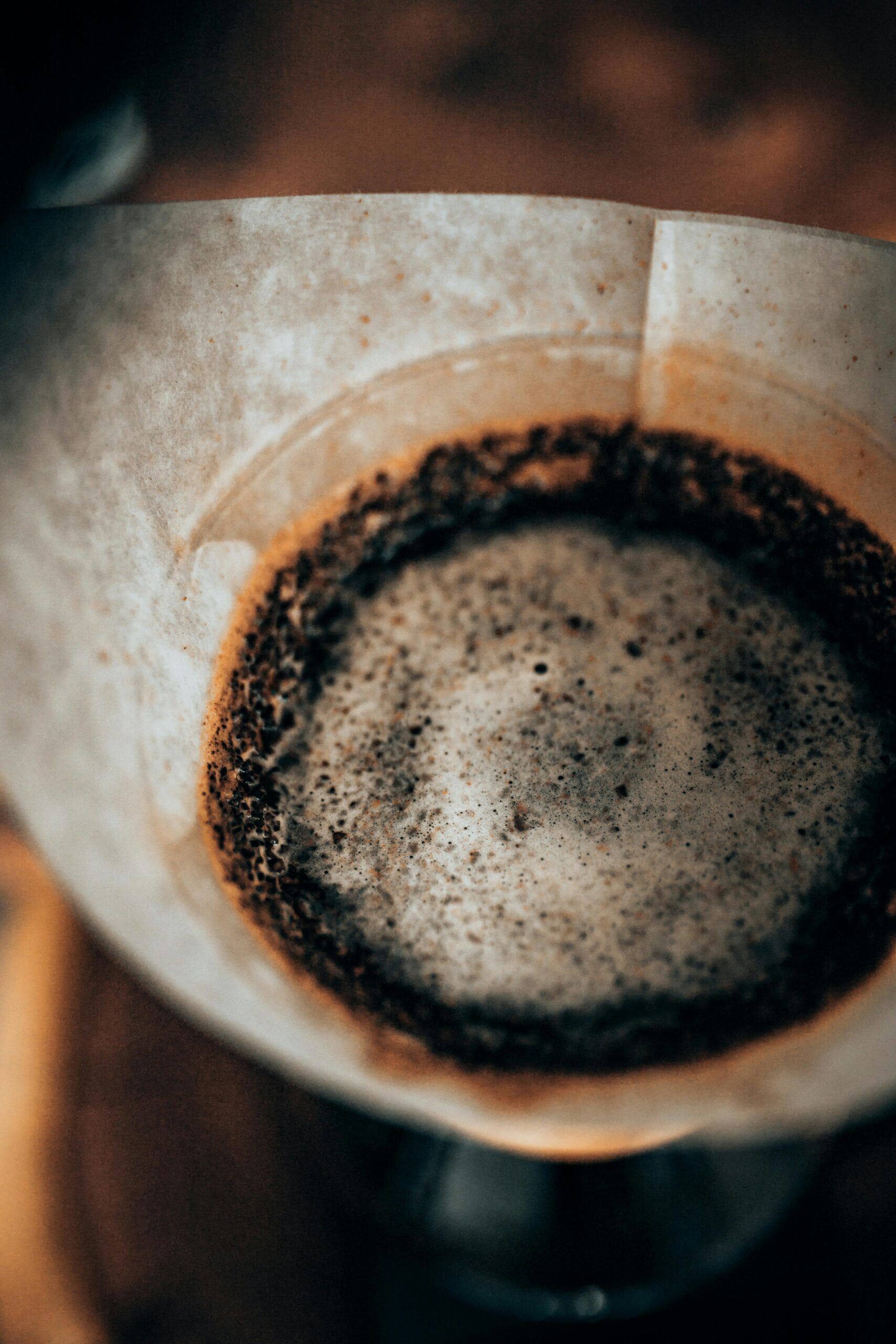 Ground coffee is placed in a paper filter, partially wet from brewing, showcasing the textured surface of the coffee grounds