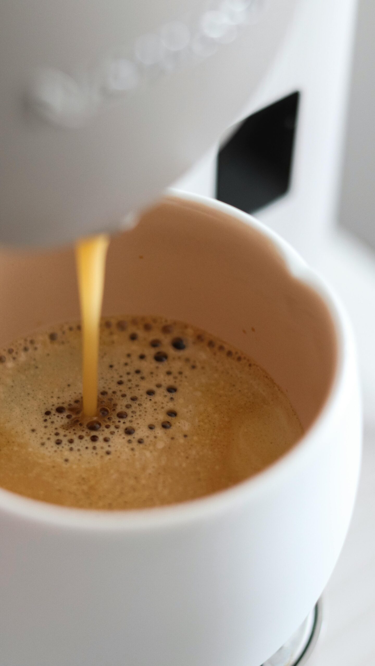Close-up of espresso being poured into a white coffee cup, with rich crema forming on the surface of the coffee